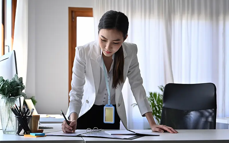 Nữ doanh nhân quyến rũ đang đứng ở bàn làm việc và kiểm tra báo cáo.