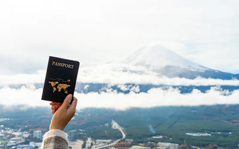 Tay người phự nữ cầm cuốn hộ chiếu (passport) đưa hướng lên trời, phía xa là dãy núi Fuji của Nhật Bản