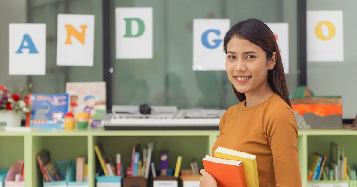 Cô giáo châu Á xinh đẹp mỉm cười với máy ảnh ở phía sau lớp học tại trường tiểu học. Những bức ảnh theo phong cách hiệu ứng cổ điển.