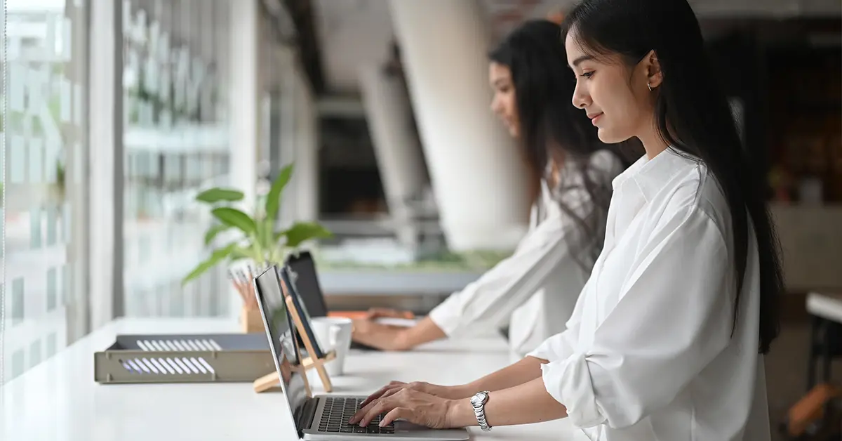 Nữ nhân viên đang mỉm cười làm việc trên laptop tại văn phòng công ty.