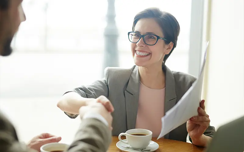 Nữ doanh nhân cầm giấy tờ chúc mừng nhân viên hoặc đối tác mới bằng cách bắt tay