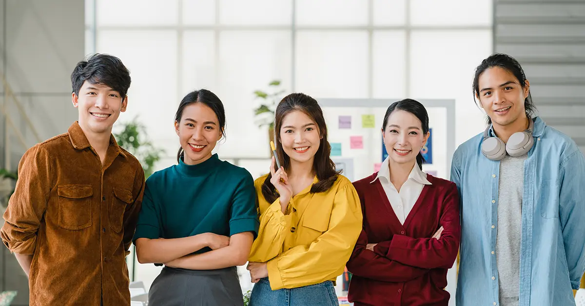Nhóm người trẻ sáng tạo Châu Á mặc trang phục giản dị, tươi cười và khoanh tay tại nơi làm việc văn phòng sáng tạo. Nam và nữ Châu Á đa dạng đứng cùng nhau tại công ty khởi nghiệp. Khái niệm làm việc nhóm đồng nghiệp.