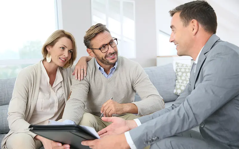 Chuyên gia đang hào hứng tư vấn cho một cặp vợ chồng vui vẻ về các vấn đề đầu tư, bảo hiểm, tài chính và chuẩn bị ký kết khi họ đang ngồi trên sofa ở phòng khách