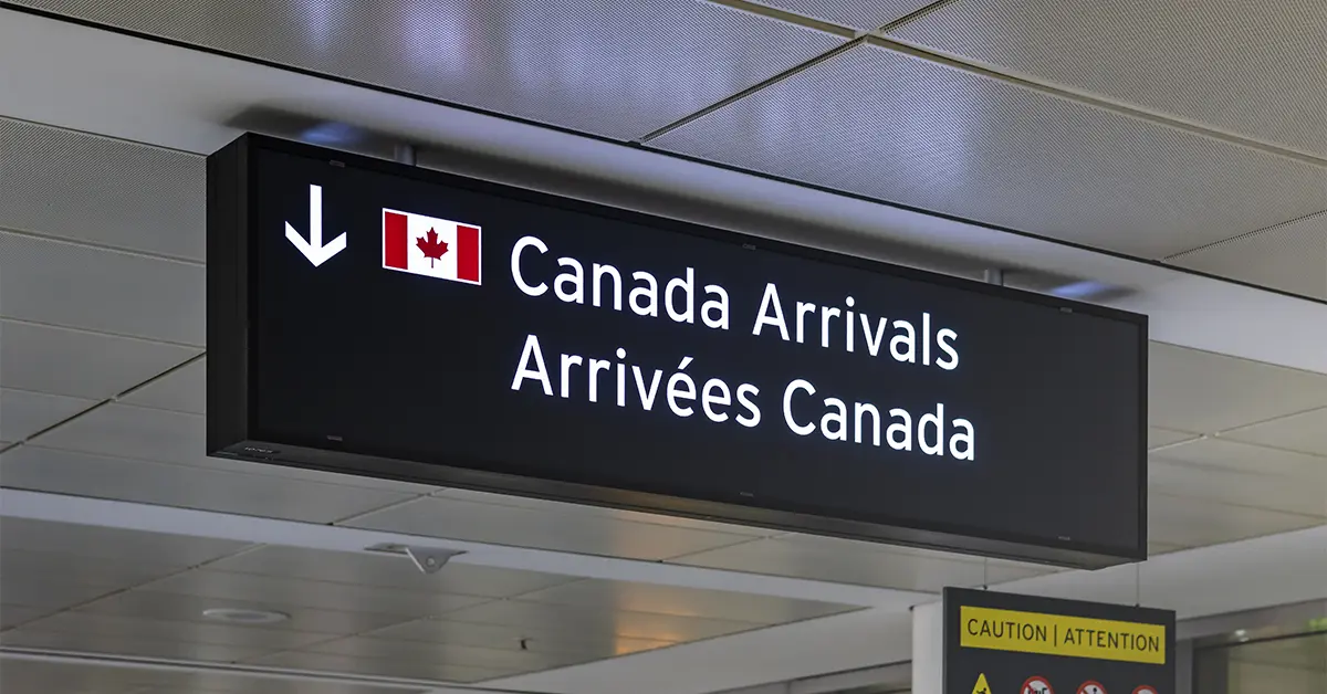 Biển báo sân bay cho biết Canada đến bằng tiếng Anh và tiếng Pháp với hình ảnh lá cờ Canada